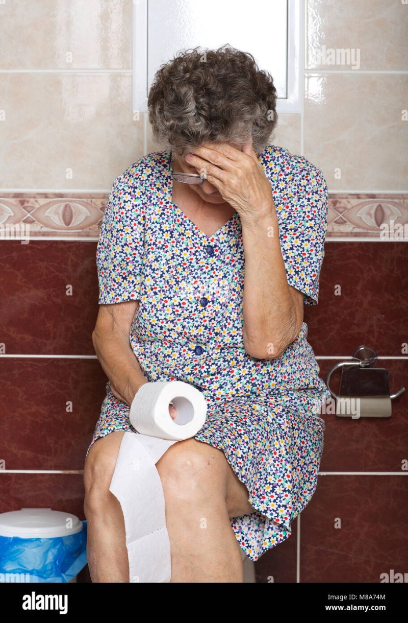 An elderly woman sits on the toilet